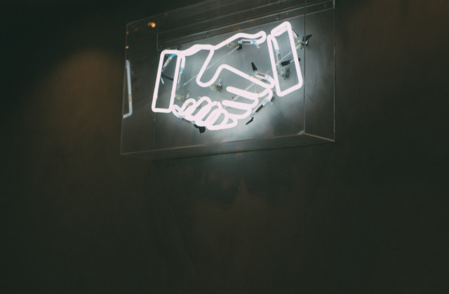 An image of a neon light showing shaking hands